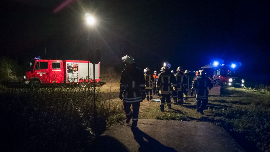 Eine Gruppe von Feuerwehrleuten steht nachts neben zwei Feuerwehrautos an der Wörnitz