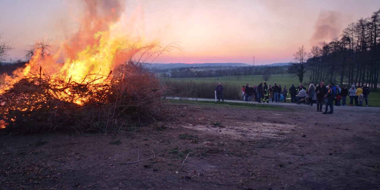 Menschen stehen am brennenden Osterfeuer in der Abenddämmerung