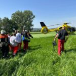 Mehrere Mitarbeiter des Rettungsdienstes sowie Feuerwehrler tragen den Patienten über eine Wiese zum Rettungshubschrauber Christoph 65